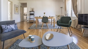 Una sala de estar moderna con un sofá, dos mesas auxiliares, un comedor con una mesa y sillas, un televisor y una estantería.