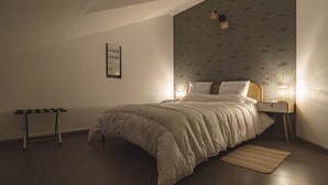 Quarto com uma cama grande, mesa de cabeceira com luminária, uma mesinha e prateleira fixada na parede.