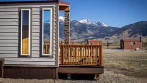 A cabin with a wooden deck and a large window, set against a backdrop of mountains. - Green Drake Tiny Home (Pray)