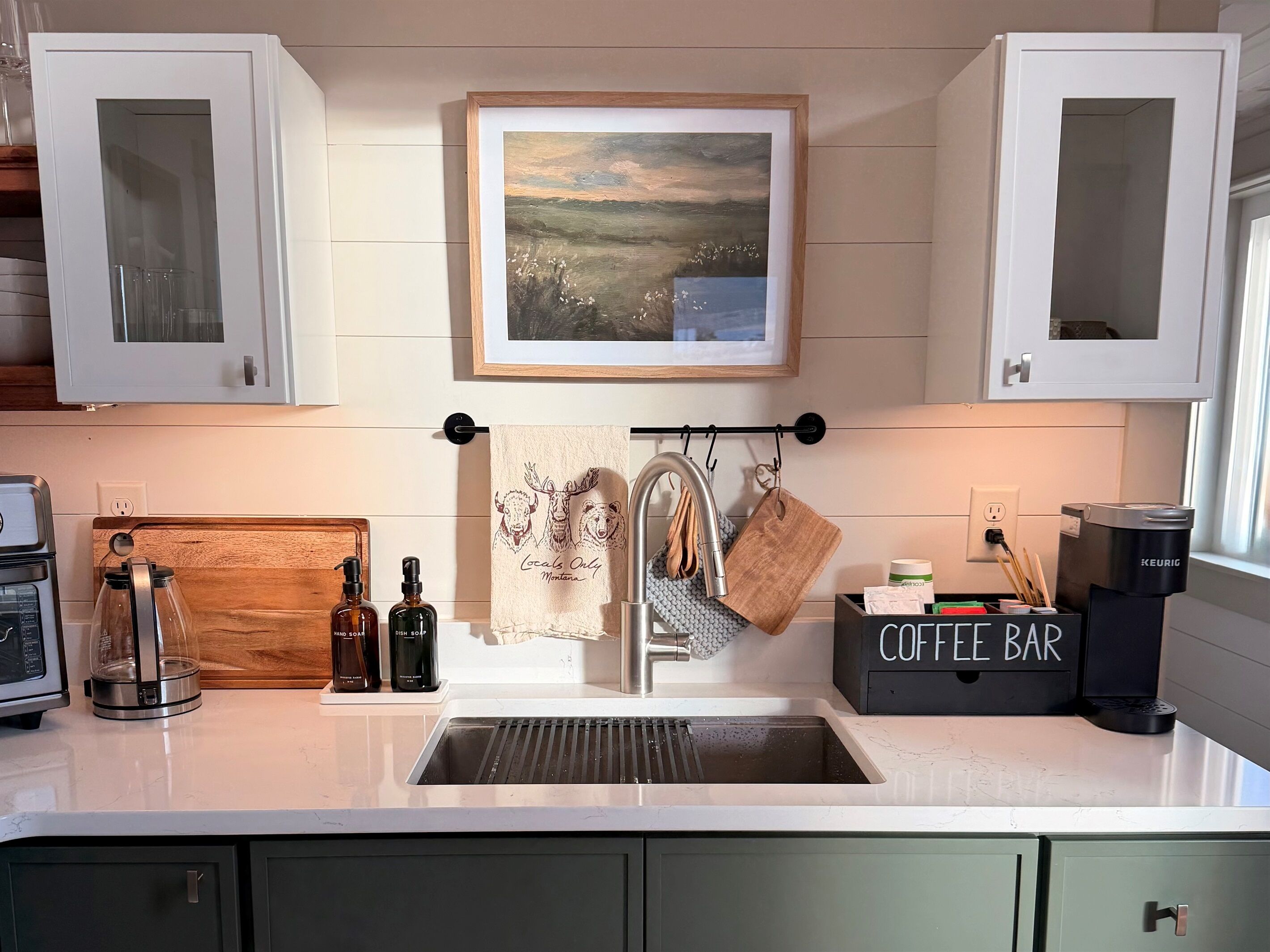 A kitchen with a sink, a coffee bar, and a painting above the sink.