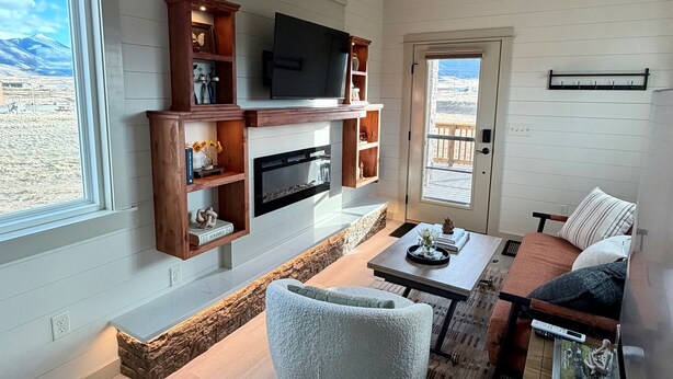 A modern living room with a fireplace, television, and seating area. - Green Drake Tiny Home (Pray)