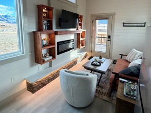 A modern living room with a fireplace, television, and seating area. - Green Drake Tiny Home (Pray)