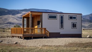 A modern cabin with a wooden deck and large windows, set against a mountainous backdrop. - Green Drake Tiny Home (Pray)