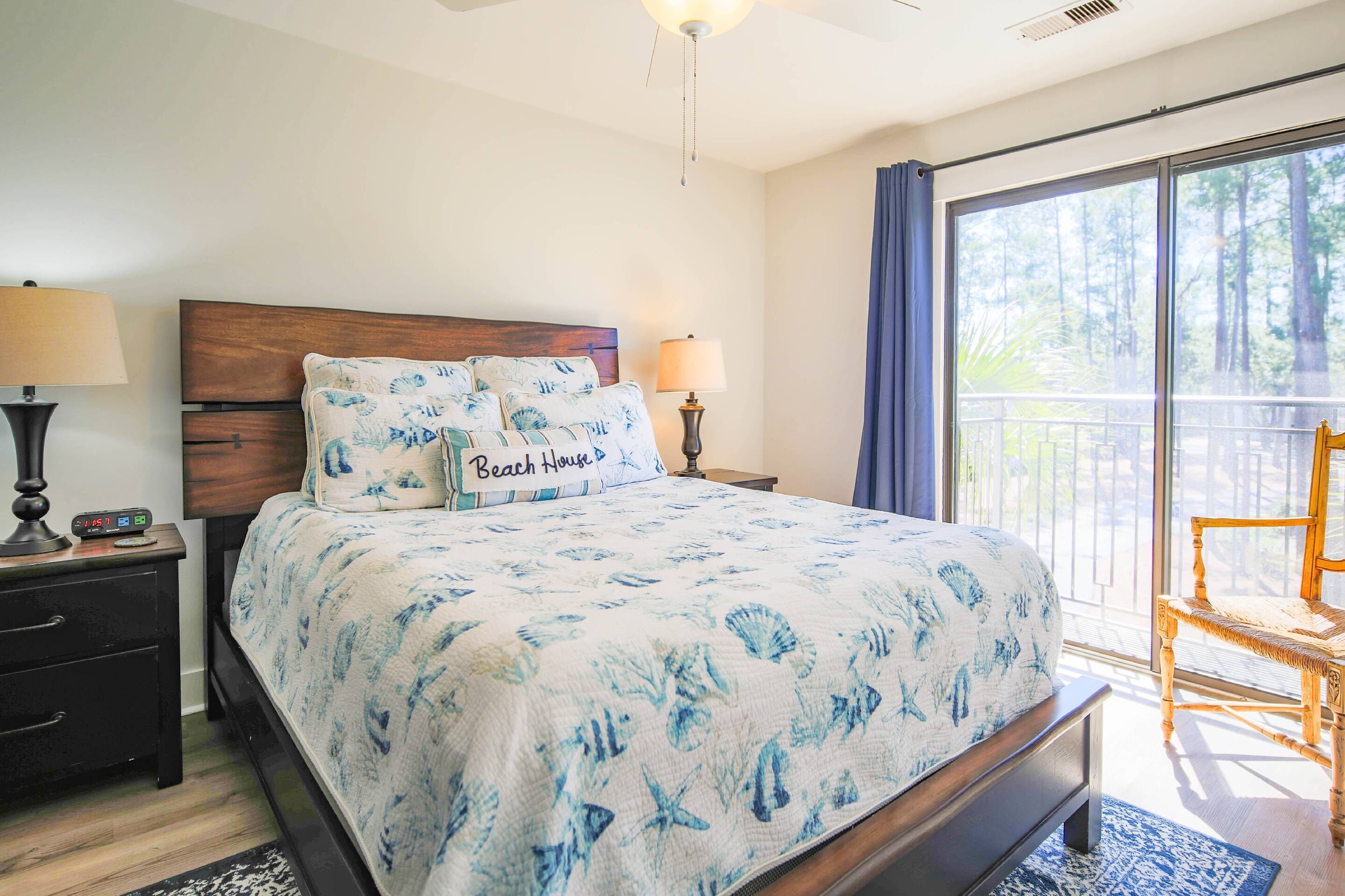 Une chambre à coucher comprenant un lit, deux tables de chevet, une commode, une chaise et une grande fenêtre donnant sur des arbres.