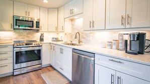 A modern kitchen with white cabinets, stainless steel appliances, and a coffee maker. - In the Heart of Harbour Town!  Gorgeous, End Unit Townhome w/ Community Pool & Outdoor Balconies! (Hilton Head Island)