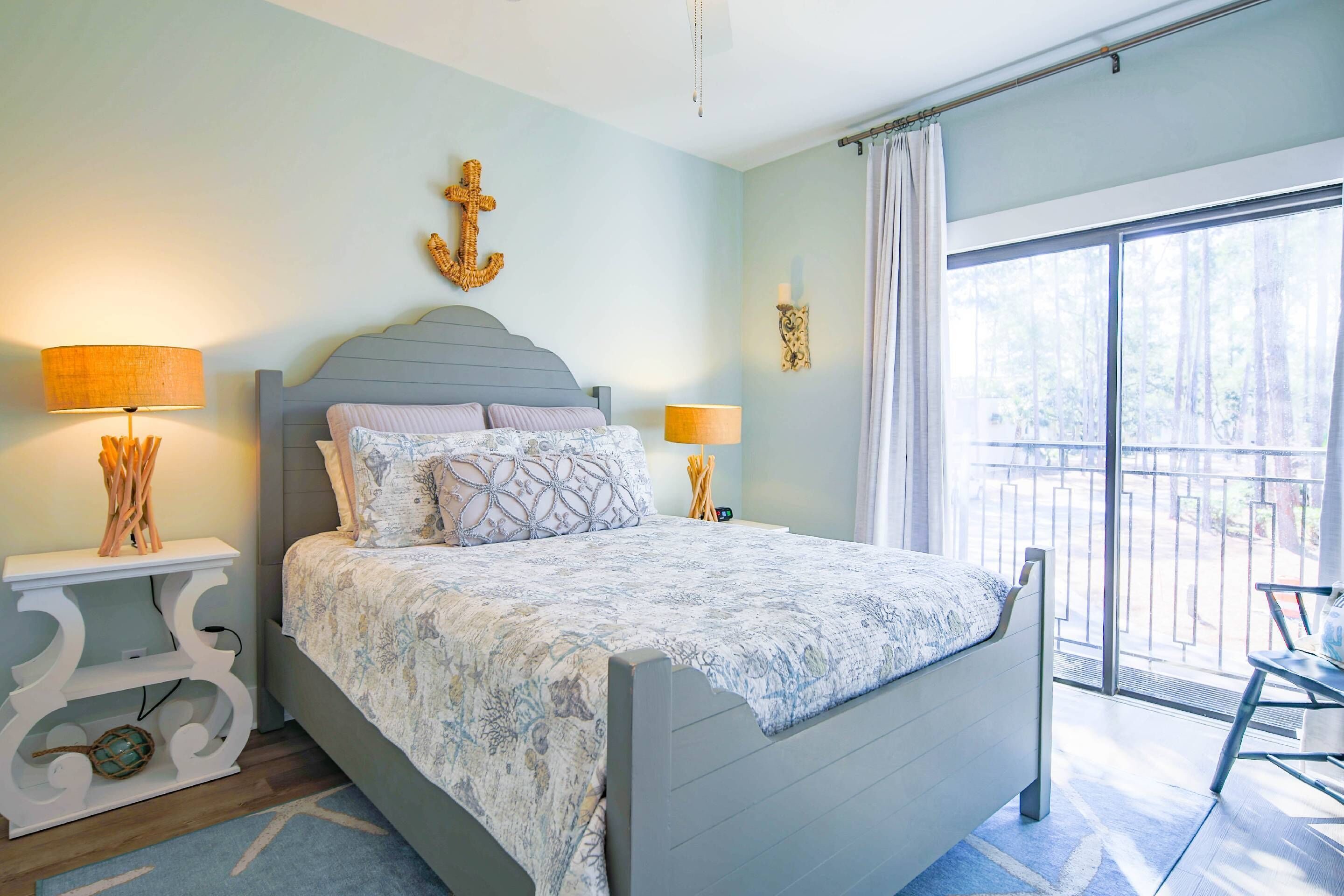 A bedroom with a bed, two bedside tables, a nightstand, a window with a view of trees, and a balcony with a chair.