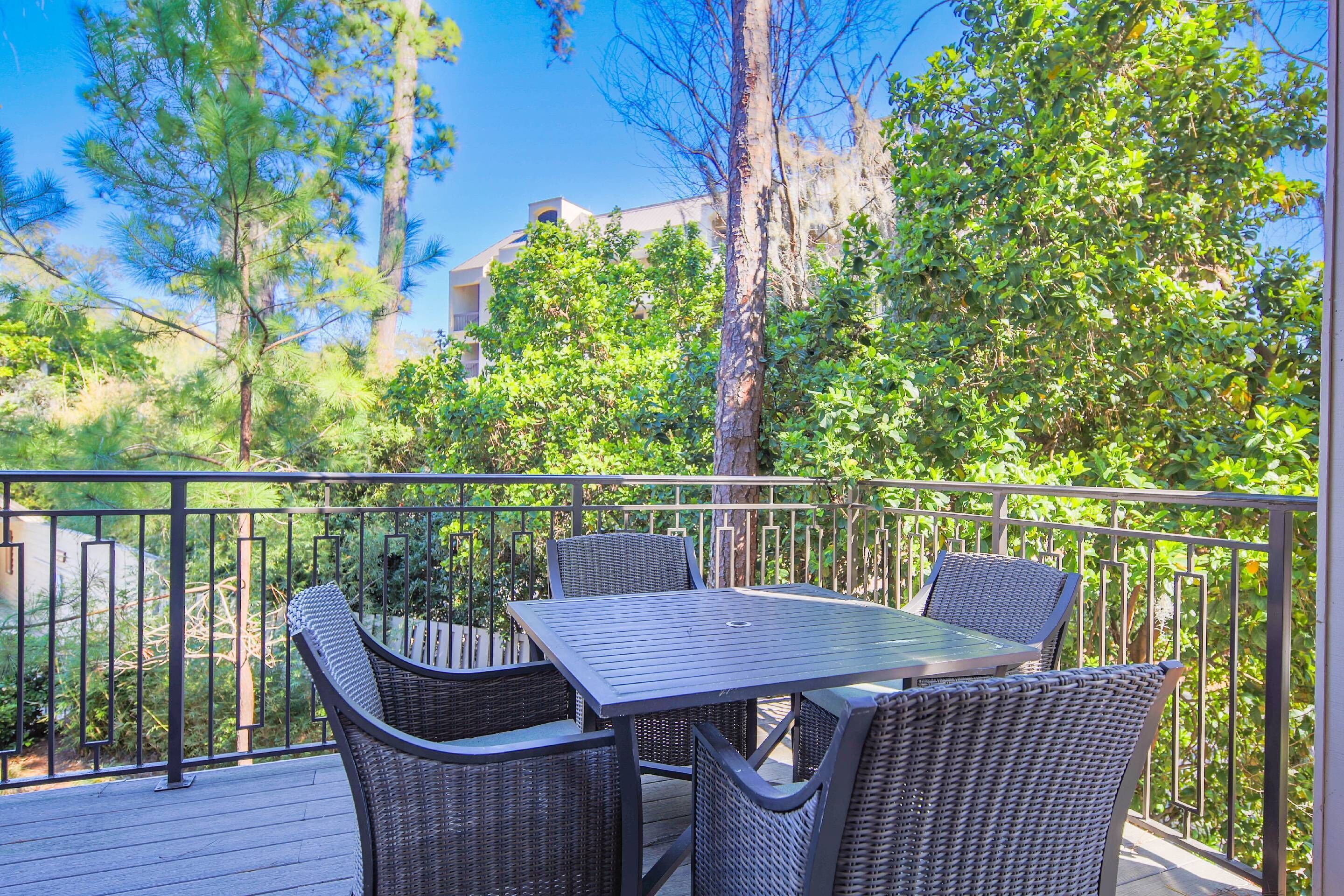 An outdoor patio with a table and four chairs, surrounded by trees and a railing.