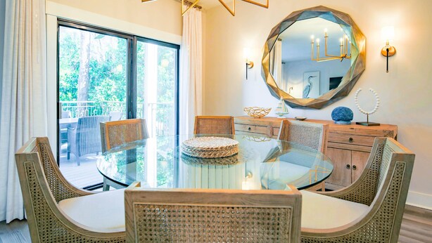 A dining area with a glass table, wicker chairs, a wooden cabinet, and a large mirror on the wall. - In the Heart of Harbour Town!  Gorgeous, End Unit Townhome w/ Community Pool & Outdoor Balconies! (Hilton Head Island)
