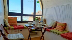 A cozy room with a window seat, a small table with cups and a vase of flowers, and a chair with a cushioned seat. - Charming apartment with balcony, pool view - 5 guests (Gruissan)