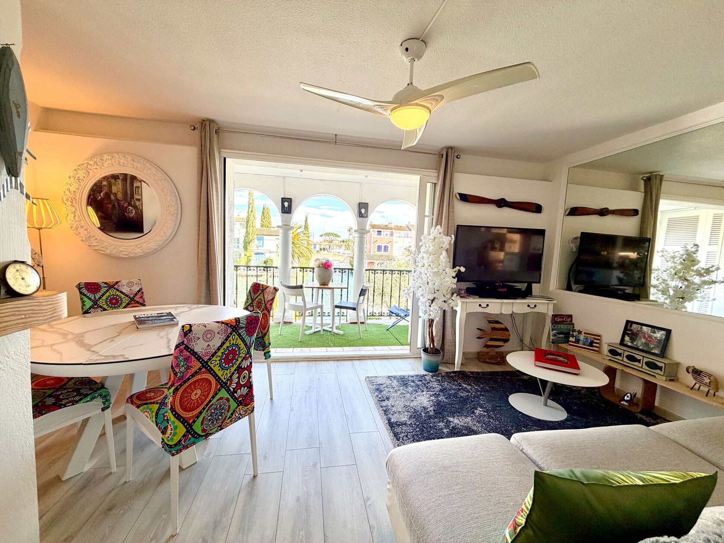 Een woonkamer met een televisie, bank en een eethoek met stoelen en een tafel.