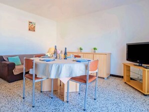 A dining area with a table set for four, a television on a stand, a sofa, and a cabinet. - T3 with AC, parking, beach nearby - 5 guests (Canet-Plage)