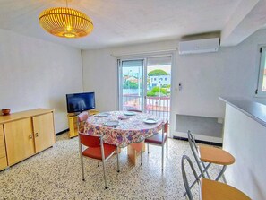 Une pièce compacte comprenant une table à manger, des chaises, un téléviseur posé sur un meuble, un buffet et un balcon avec vue.
