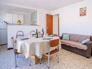 A dining area with a table set for four, a brown sofa, and a kitchen in the background. - T3 with AC, parking, beach nearby - 5 guests (Canet-Plage)