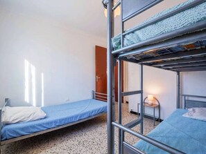 Une chambre de dortoir avec des lits superposés, une petite table de chevet avec une lampe et une porte donnant sur une autre pièce.