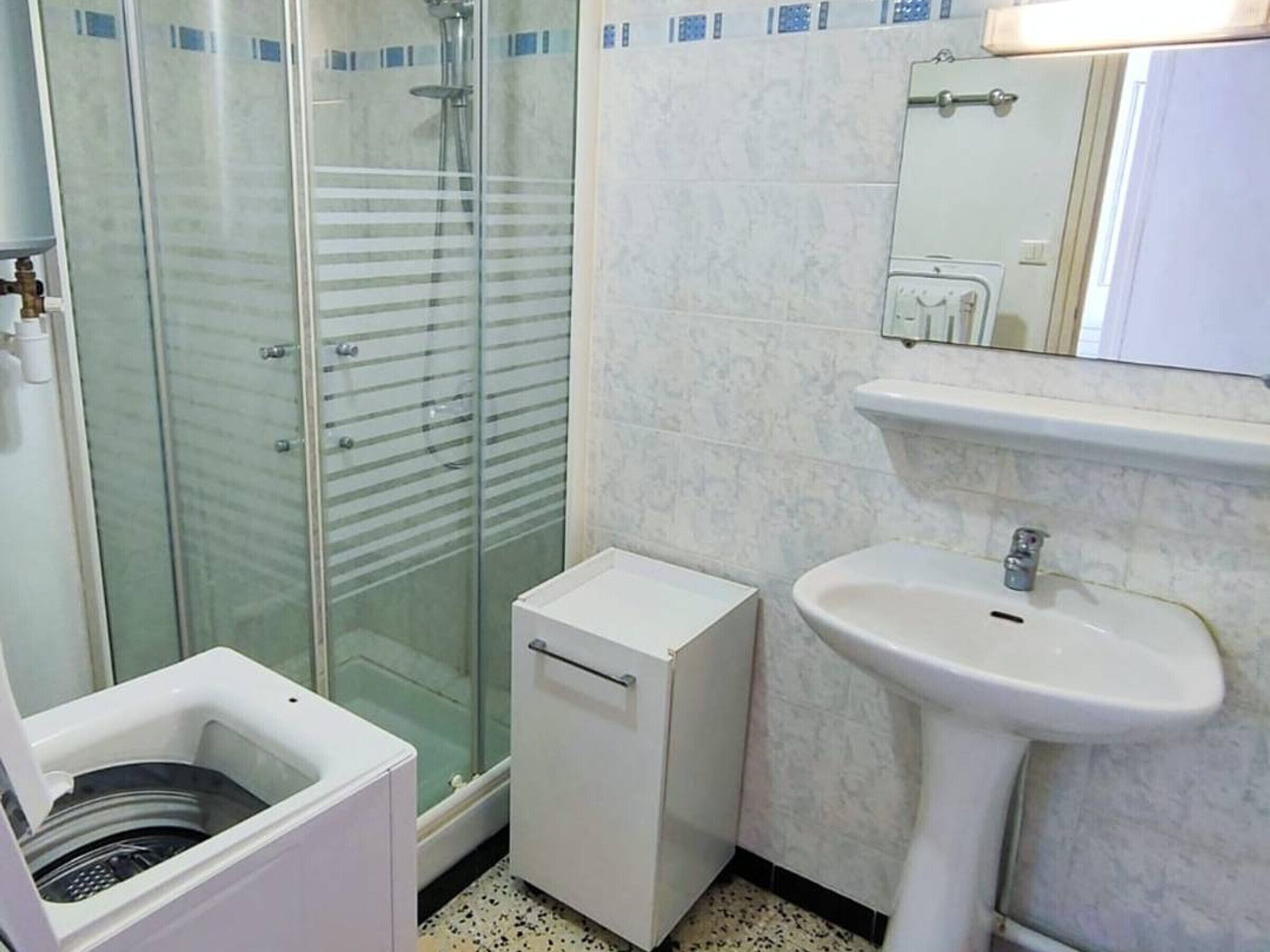 Un baño con ducha de vidrio, un lavabo blanco y una lavadora pequeña.