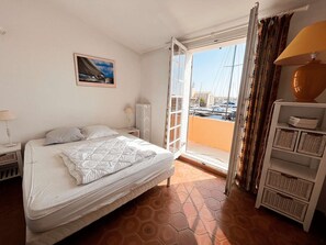 Habitación de hotel con cama, ventana con vista a barcos, un radiador y una lámpara.