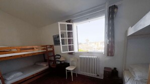 Una camera del dormitorio con letti a castello, termosifone, sedia e finestra con tende.