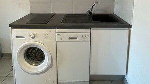 A compact kitchen with a built-in washer and dryer, a black countertop, and a stainless steel range hood.