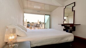 A hotel room with a bed, a bedside lamp, a mirror, and a view of the outdoors.
