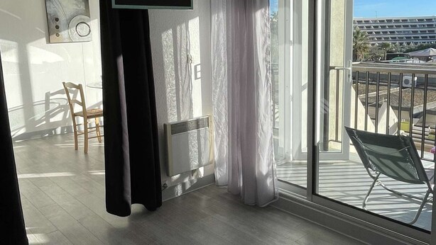 Uma sala de estar moderna com uma grande porta de vidro deslizante para uma varanda, uma TV de tela plana na parede e piso de madeira.