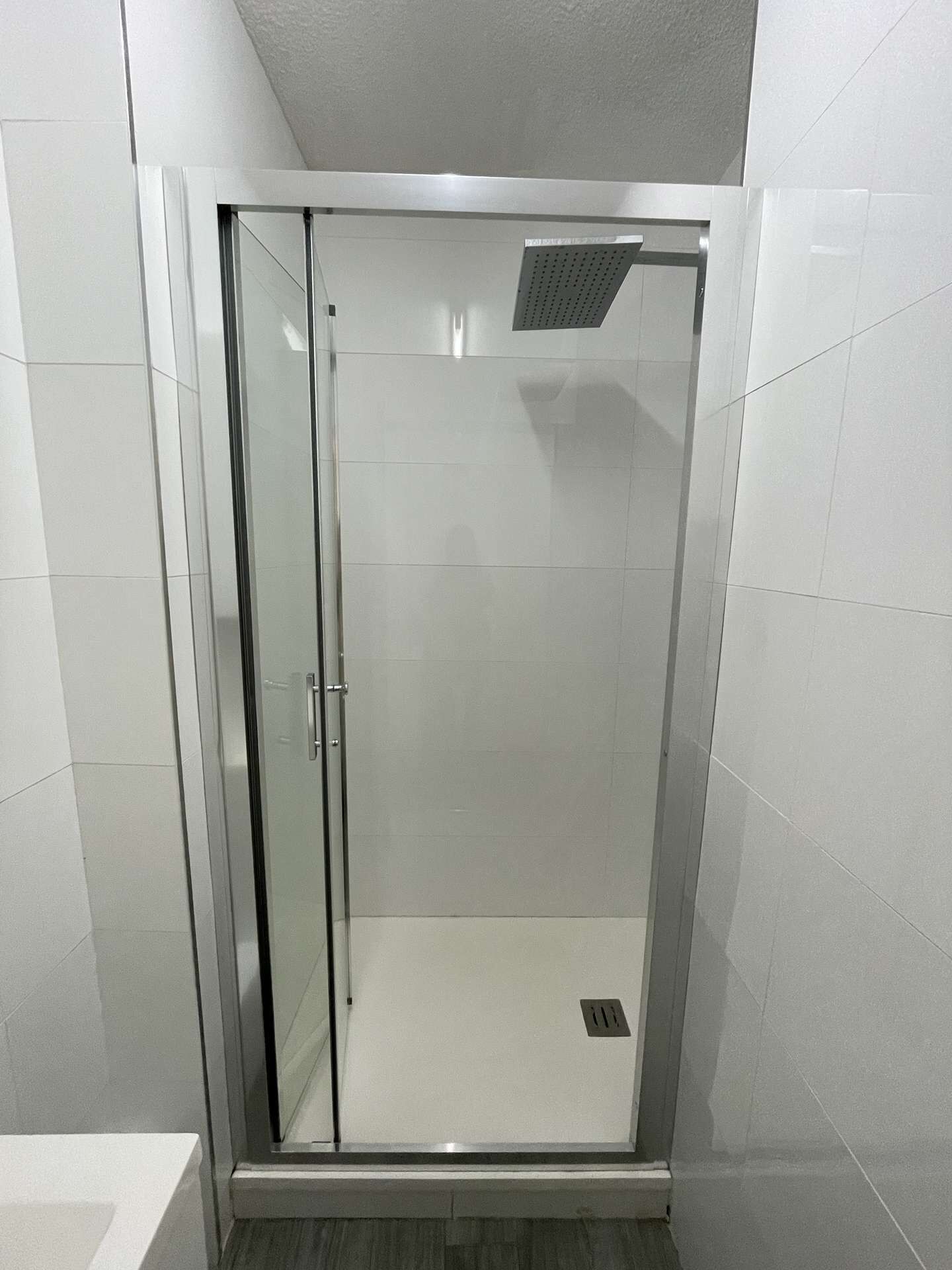 Une cabine de douche fermée par des parois en verre, avec un sol carrelé et une bouche d’aération au plafond.