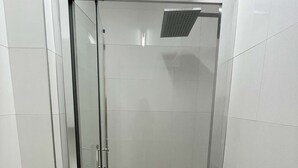 Divisória de chuveiro envidraçada com piso ladrilhado e um respiradouro no teto.