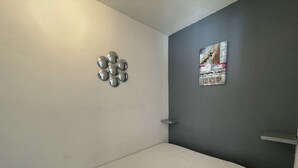 Quarto pequeno com cama de solteiro, uma cama branca, parede com detalhes em cinza e um pôster.