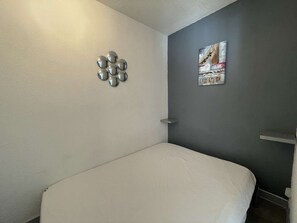 Ein kleines Zimmer mit einem Einzelbett, einem Bett in Weiß, einer grauen Akzentwand und einem Bild.