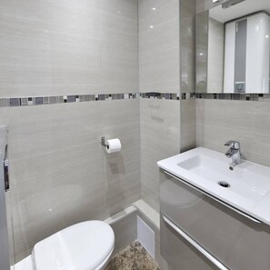Uma casa de banho moderna com sanita, lavatório e chuveiro.