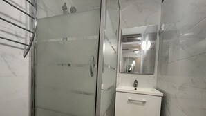 Een badkamer met een glazen douchecabine, een wit wastafelmeubel met een spiegel erboven en muren met een marmerprint.