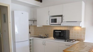 Een kleine keuken met witte kastjes, een magnetron, een broodrooster en een koelkast.