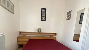 Een slaapkamer met een houten hoofdbord, een rode sprei, een bedlampje en een klein plankje met een lamp.