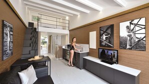 Eine moderne Küche mit einer Frau am Spülbecken, einem Essbereich mit einer schwarzen Couch und einem Fernseher auf einer Arbeitsplatte.
