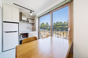 A modern kitchen with a dining table, a built-in oven, and a view of a balcony with a railing. - Samcheok The Ggeullim Pension (Samcheok)