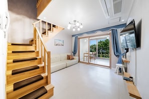 A modern interior with a wooden staircase, a sofa, a dining area, and a TV mounted on the wall. - Samcheok The Ggeullim Pension (Samcheok)