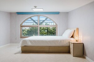 A bedroom with a large arched window, a bed with a wooden headboard, and a bedside table with a lamp.