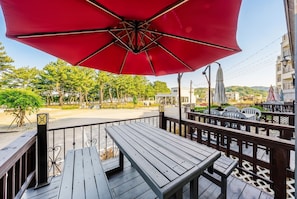 A wooden deck with a red umbrella, metal railings, and a view of a road and buildings. - Samcheok The Ggeullim Pension (Samcheok)
