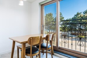 A room with a wooden table and two chairs, a sliding glass door to a balcony with a metal railing, and a light fixture on the ceiling. - Samcheok The Ggeullim Pension (Samcheok)