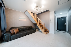 A modern living room with a sofa, a wooden staircase, and a door marked with the number 303. - Samcheok The Ggeullim Pension (Samcheok)