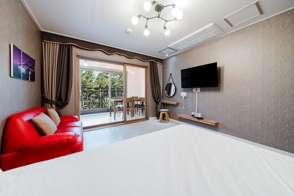 A hotel room with a red sofa, a bed, a TV mounted on the wall, and a balcony with a table and chairs. - Samcheok The Ggeullim Pension (Samcheok)