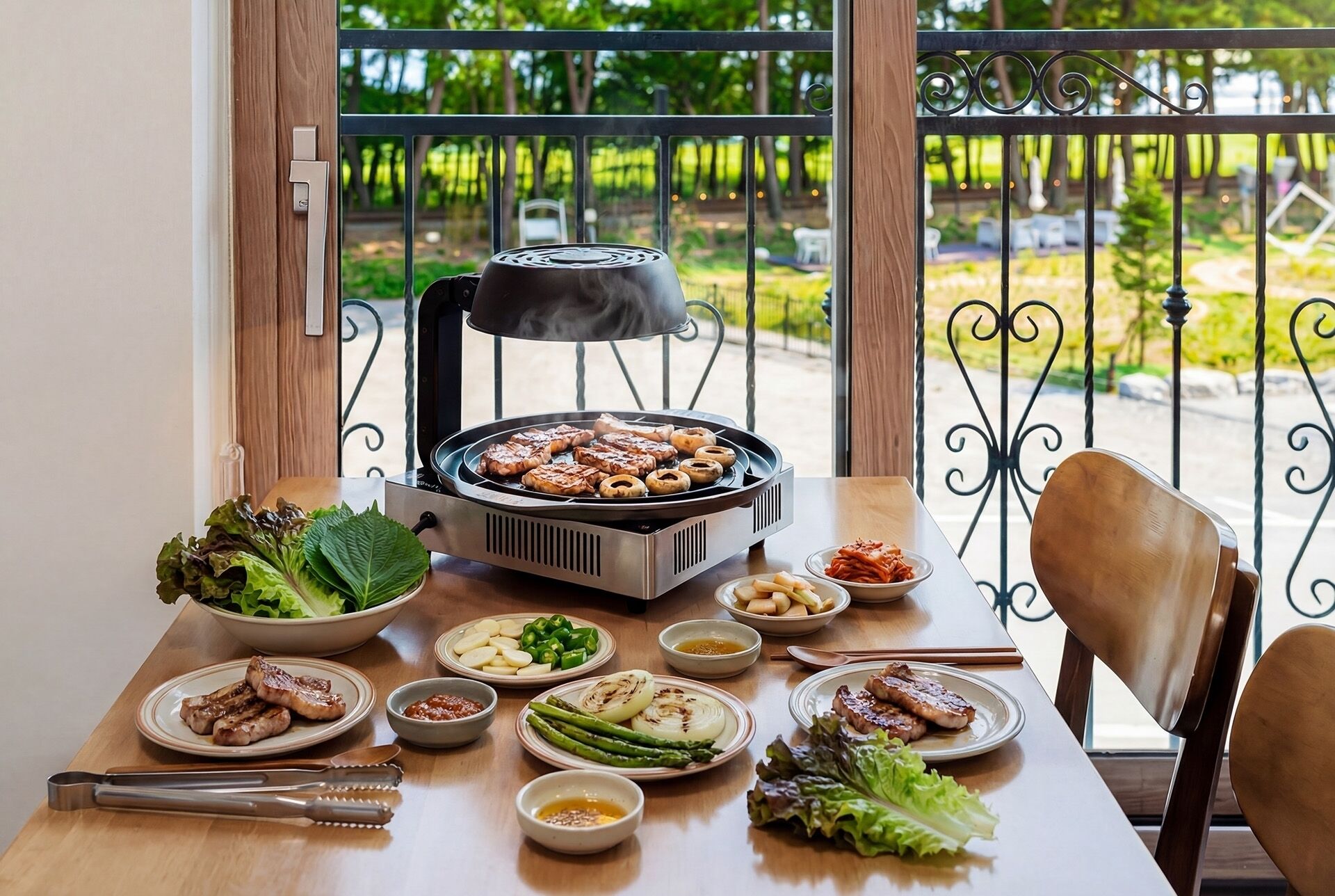 A dining table with a grill, various dishes, and a view of a garden through a balcony.