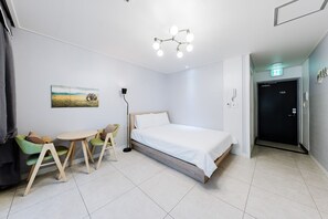 A hotel room with a bed, a desk with chairs, a painting on the wall, and a door with a number. - Samcheok The Ggeullim Pension (Samcheok)