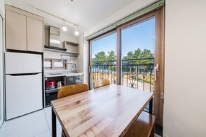 A modern kitchen with an LG refrigerator, a wooden dining table, and a balcony with a view of trees and a body of water. - Samcheok The Ggeullim Pension (Samcheok)