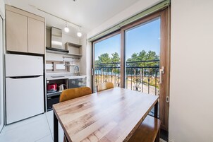 A modern kitchen with an LG refrigerator, a wooden dining table, and a balcony with a view of trees and a body of water.