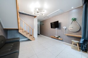 A modern living room with a wooden staircase, a flat-screen TV, a round mirror, and a small stool. - Samcheok The Ggeullim Pension (Samcheok)