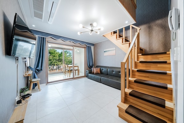 A modern living room with a sofa, a dining table, and a staircase. - Samcheok The Ggeullim Pension (Samcheok)