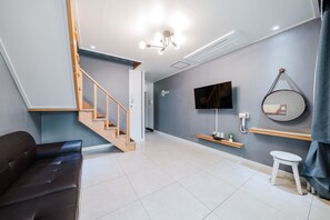 A modern living room with a staircase, a flat-screen TV, a mounted mirror, and a small table with a plant. - Samcheok The Ggeullim Pension (Samcheok)