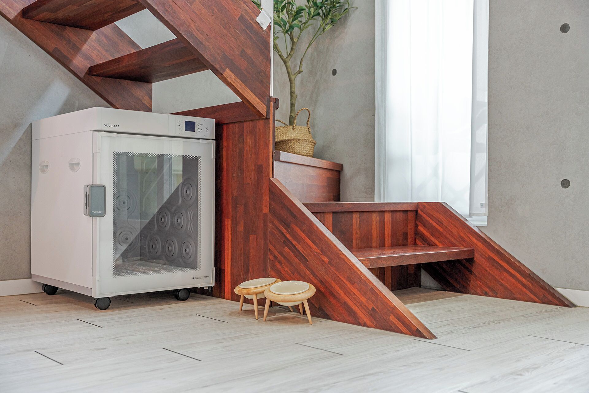 A modern room with a built-in refrigerator, a wooden staircase, and a small seating area with stools.