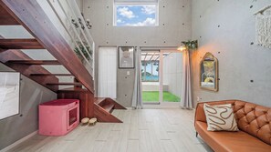 A modern interior with a staircase, a pink pet bed, a leather sofa, and a view through a glass door. - Taean Badameong Pet Pool Villa (Taean)