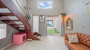 Un interior moderno con una escalera, una cama para mascotas color rosa, un sofá de cuero y vistas a través de un ventanal.